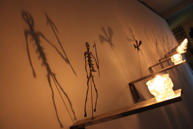 Metal sculptures of skeletons casting shadows on a wall